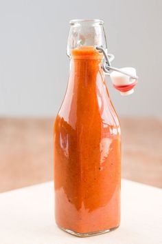 a glass bottle filled with sauce sitting on top of a wooden table next to a spoon