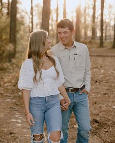 a young man and woman standing in the woods holding hands, looking at each other