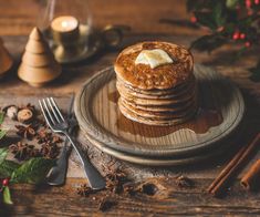 a stack of pancakes sitting on top of a wooden plate next to some cinnamons