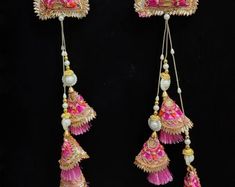 two pink and gold earrings with tassels hanging from the side on a black background