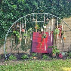 an arch with plants hanging from it in front of a brick wall and green foliage