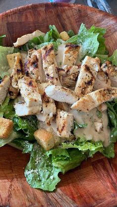 a wooden bowl filled with chicken and lettuce covered in dressing on top of a table