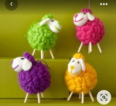 four small sheep are hanging from clothes pins on a green wall, one is multicolored and the other is white