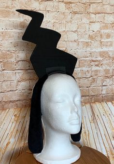 a white mannequin head with a black hat on it's head and a brick wall in the background