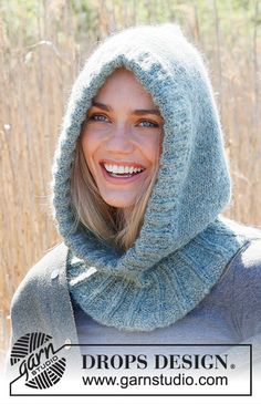 a woman wearing a hood and smiling for the camera in front of some tall grass