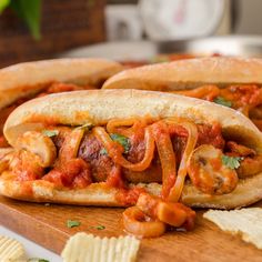 two hot dogs with tomato sauce, cheese and chips on a cutting board next to a bowl of crackers