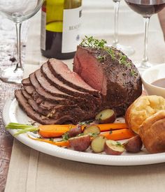 a white plate topped with meat and veggies next to two glasses of wine