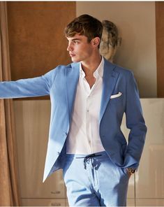 a man in a blue suit and white shirt leaning against a wall with his hand out