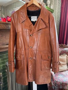 Made in Canada by Victoria Leather, this heavier weight coat is a classic shade of medium caramel brown leather that feels soft and supple. It has the original buttons in the front and on the pockets, cuffs and back belt detail; two outer pockets; and a half belt in the back. The dark brown faux fur lining can be removed and re-attached as the weather changes. Marked size 46. The measurements, taken with the coat lying flat, are: shoulder to shoulder, 20 inches; armpit to armpit, 23 inches; sleeves, 25 1/2 inches; length, 37 inches; bottom edge, 36 inches. In very good condition. Vintage Outerwear, Weather Change, Caramel Brown, Brown Leather Jacket, Trench Coats, Jacket Coat, Leather Coat, Vintage Men, Red Leather Jacket