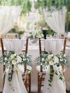 the chairs are decorated with white flowers and greenery