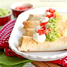 a burrito with guacamole and tomatoes on it sitting on a white plate