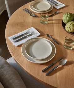 a wooden table topped with white plates and silverware