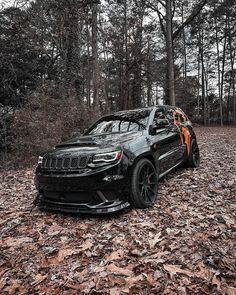 a black jeep parked in the woods with its hood up and paint job on it