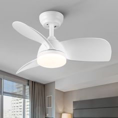 a white ceiling fan in a bedroom with a large window behind it and a lamp on the side