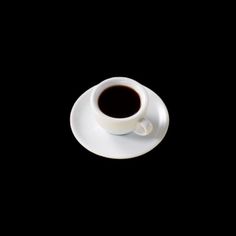 a cup of coffee sitting on top of a saucer next to a black background