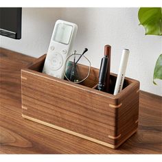 a wooden pen holder with pens, glasses and remotes in it on a desk