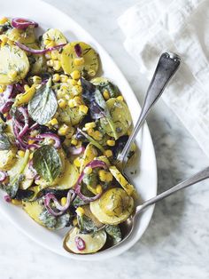 a white plate topped with corn and other vegetables next to a napkin on top of a marble counter