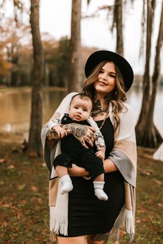 a woman holding a baby in her arms while standing next to some trees and water