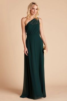 a woman in a long green dress with one shoulder draped over her shoulders and gold clutch