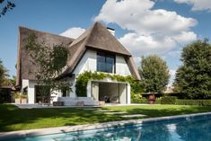 a house with a thatched roof next to a swimming pool in front of it