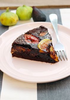 a piece of cake on a plate with a fork and some fruit in the background