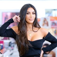 a woman with long dark hair wearing a black dress and gold necklace, posing for the camera