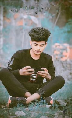 a young man sitting on the ground looking at his cell phone while holding something in his hand