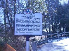 a sign on the side of a road near some snow covered ground and trees in the background