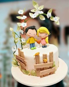 a cake with two people on top of it and flowers around the edges, sitting on a table