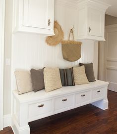 a white bench with several pillows on it and a basket hanging from the wall above