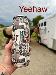 a person holding up a can of beer in front of a horse trailer