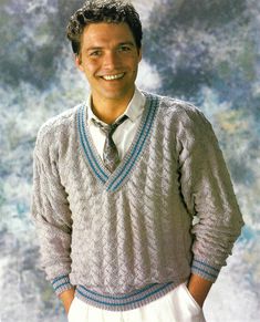 a man wearing a sweater and tie smiling at the camera with his hands in his pockets