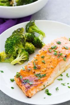 a white plate topped with salmon and broccoli next to a bowl of broccoli