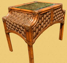 a small table with a glass top and wicker design on the bottom, sitting in front of a white background