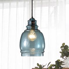 a blue glass light hanging from a ceiling in front of a window with white curtains