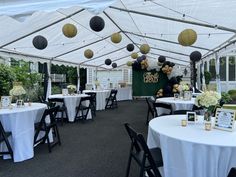 tables and chairs are set up under a white tent with black and gold decorations on it