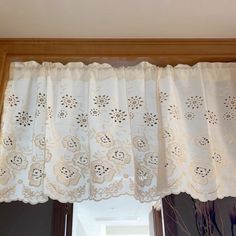 a window with white curtains and flowers on the valance, in front of an open window