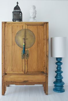 a wooden cabinet sitting next to a lamp on top of a white floor covered in blue vases