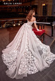 a woman in a wedding dress is sitting on a red chair and looking at the piano