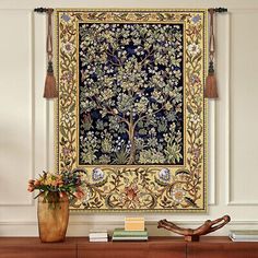 an ornate tapestry hangs on the wall above a table with flowers and books in front of it