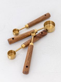 three brass measuring spoons with wooden handles on a white surface, next to each other