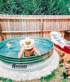 a woman wearing a hat sitting in an outdoor hot tub with two dogs beside her