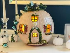 a pumpkin shaped like a house with windows and flowers on it, surrounded by candles