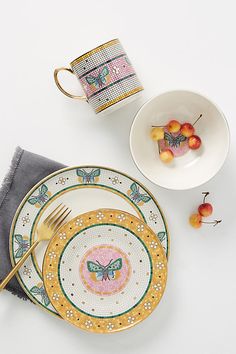 a white table topped with plates and bowls filled with fruit next to a cup on top of a saucer