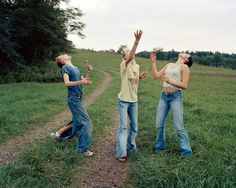 three people standing on a dirt road with their arms in the air and one person reaching up