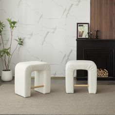 two white stools sitting next to each other in front of a fireplace with a potted plant