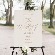 a welcome sign with flowers and greenery sits on an easel in the middle of a path