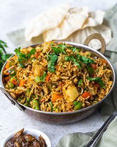 a bowl filled with rice and vegetables next to some silver spoons on a table