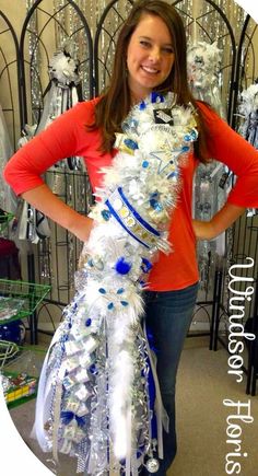 a woman standing in front of a display of white and blue flowers with ribbons around her neck