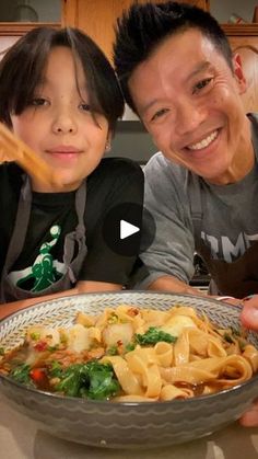 a man and boy are smiling while holding a bowl of food in front of them